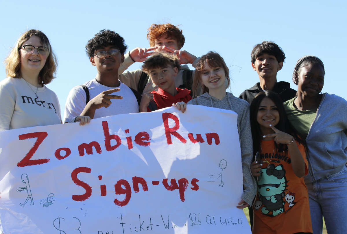 Key Club members Ella Quinney (11) and Lorelei Wise (11) gather around the Zombie Run sign, surrounded by other students. 